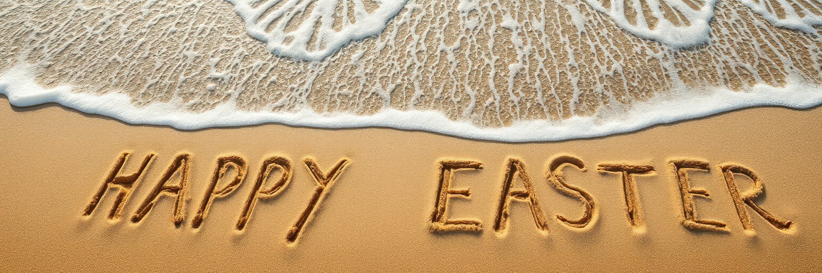 Happy Easter message written in sand near ocean waves on a sunny beach